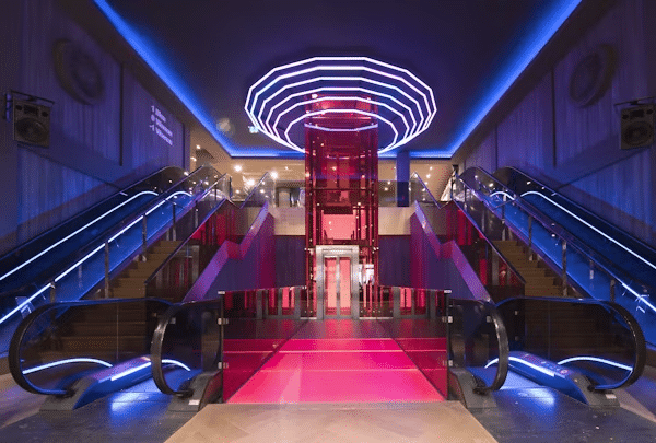 image Futuristic entrance hall with illuminated escalators and central elevator in a vibrant, modern building interior. | Sky Rye Design Futuristic entrance hall with illuminated escalators and central elevator in a vibrant, modern building interior.
