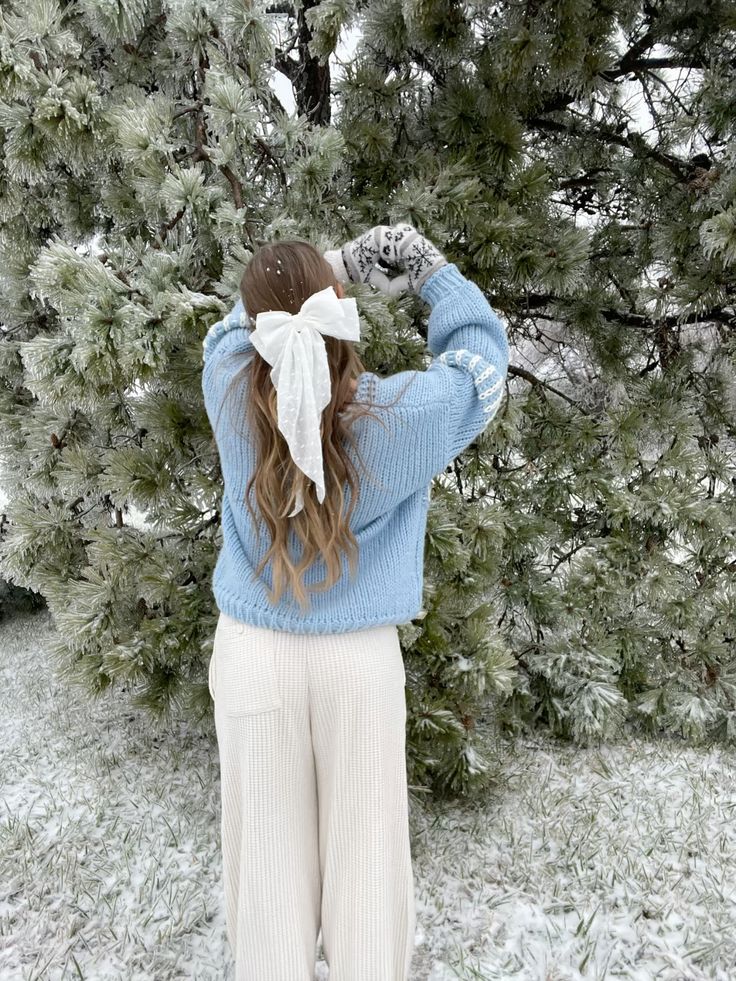 in a winter wonderland ❄️☃️💙 Woman in blue sweater and white pants admires snowy pine trees, wearing gloves and a hair bow. Winter scene. | Sky Rye Design Woman in blue sweater and white pants admires snowy pine trees, wearing gloves and a hair bow. Winter scene.