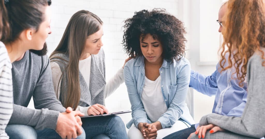 Support group comforting a member in distress during a meeting, fostering empathy and mental health awareness.
