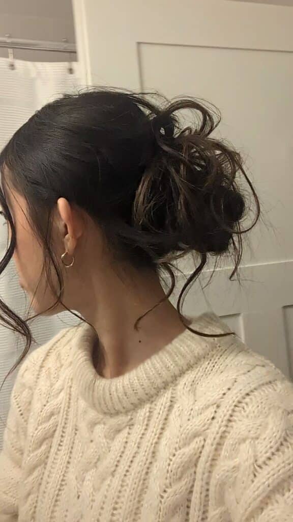 Woman with messy bun hairstyle and cozy sweater, view from the side in a bathroom setting.