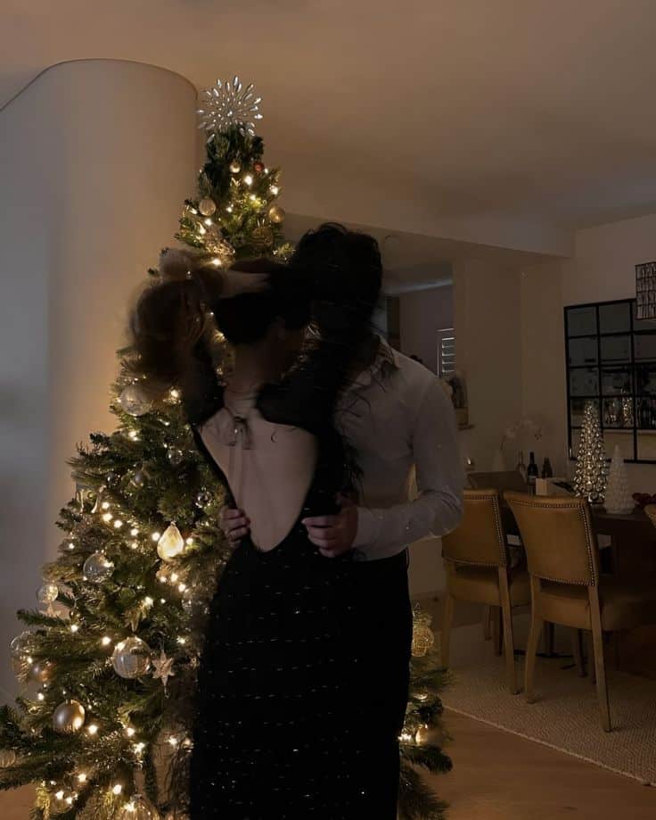 Couple dancing by a decorated Christmas tree in warm lighting, creating a festive and intimate holiday atmosphere.