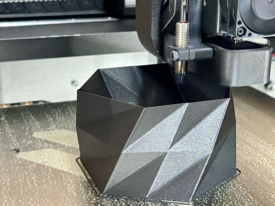 pantheon-hs3-print-vase-1 3D printer creating a black, geometric-patterned object on a textured surface. | Sky Rye Design 3D printer creating a black, geometric-patterned object on a textured surface.