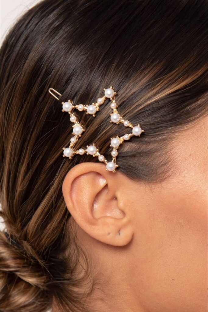 Woman with hairpin styled as pearl-studded star, worn above ear in sleek, elegant hairstyle.