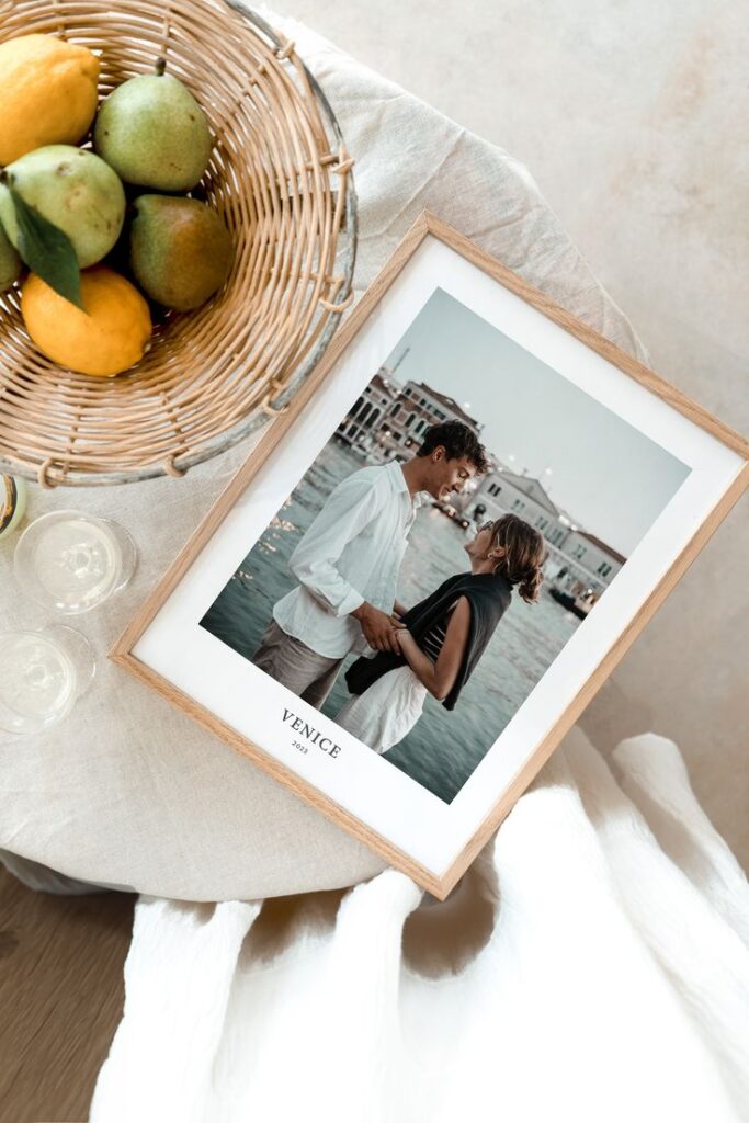Framed photo of a couple labeled Venice 2023 on table with fruit basket and drinks.