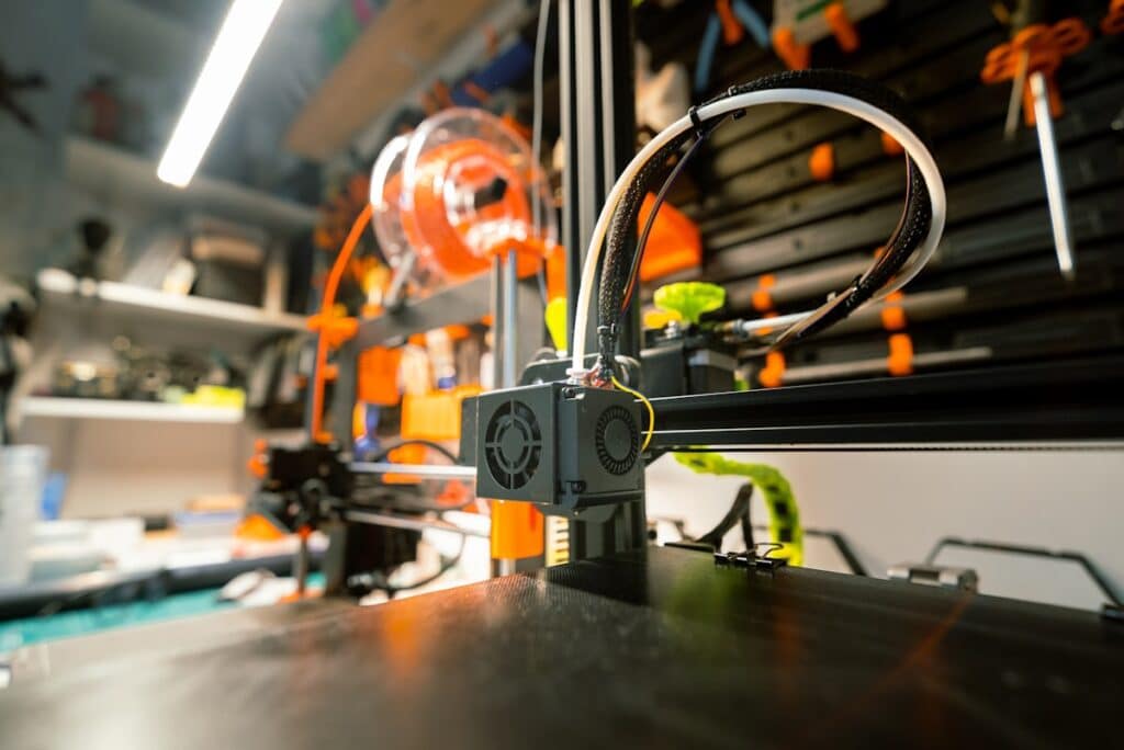 Close-up of a 3D printer in action, with orange filament and detailed components visible in a workshop setting.
