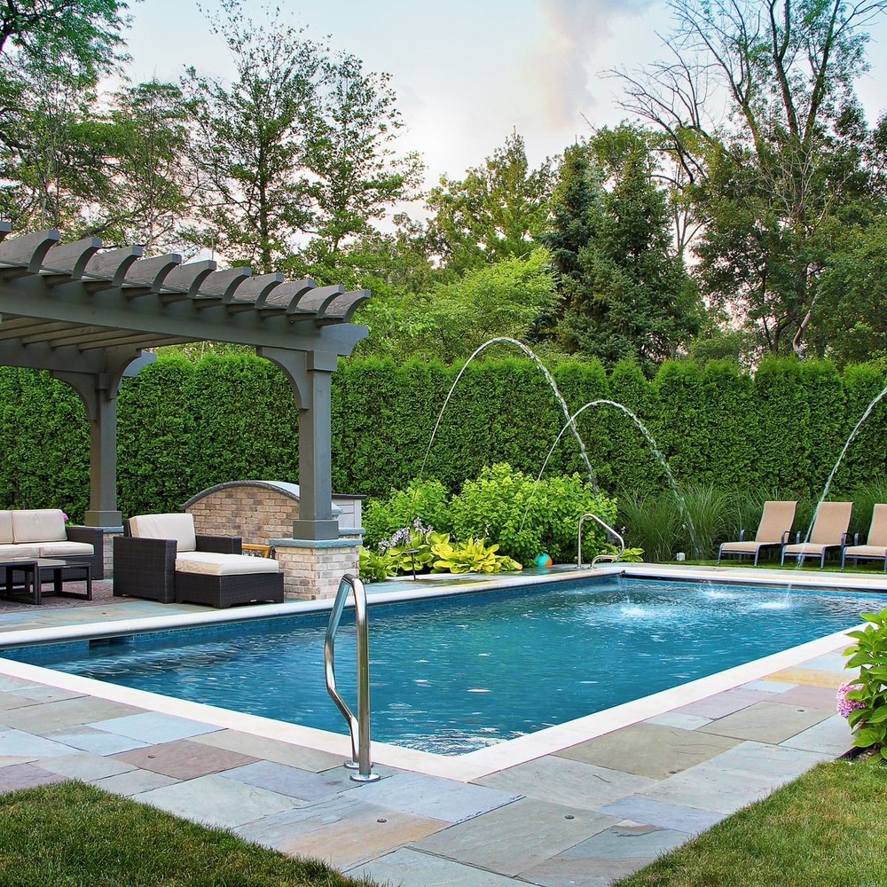 pool-with-water-features-and-a-pergola Backyard oasis with a rectangular swimming pool, pergola, lounge chairs, and lush greenery for relaxation and enjoyment. | Sky Rye Design Backyard oasis with a rectangular swimming pool, pergola, lounge chairs, and lush greenery for relaxation and enjoyment.