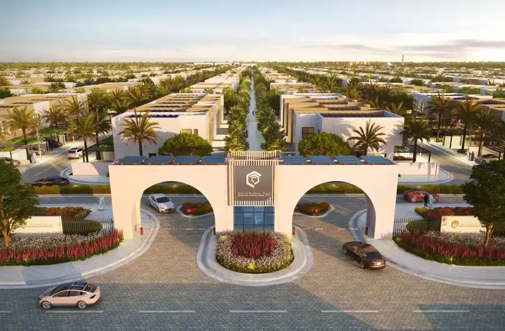 Modern residential community entrance with solar rooftops and palm-lined streets under a clear blue sky.
