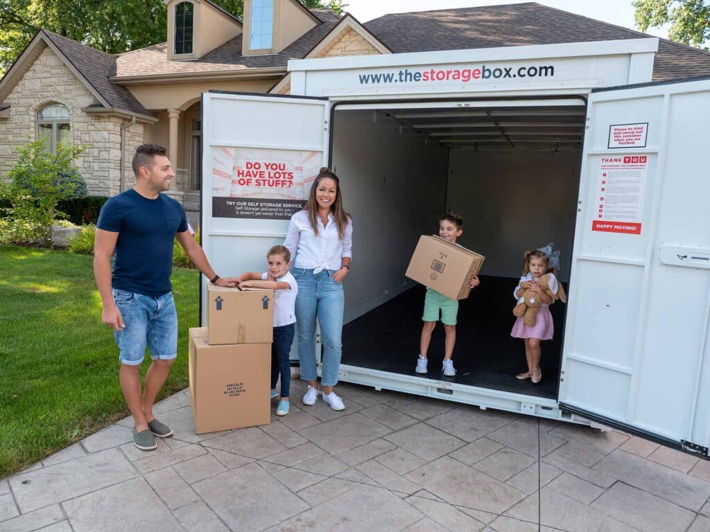 storage-box-stills-4 Family moving boxes into a storage unit with kids, house in background. | Sky Rye Design Family moving boxes into a storage unit with kids, house in background.