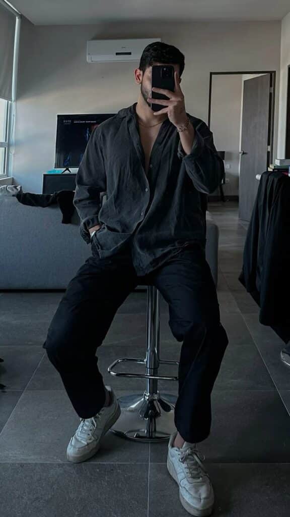 Man in dark casual outfit takes mirror selfie in modern living room, seated on bar stool.