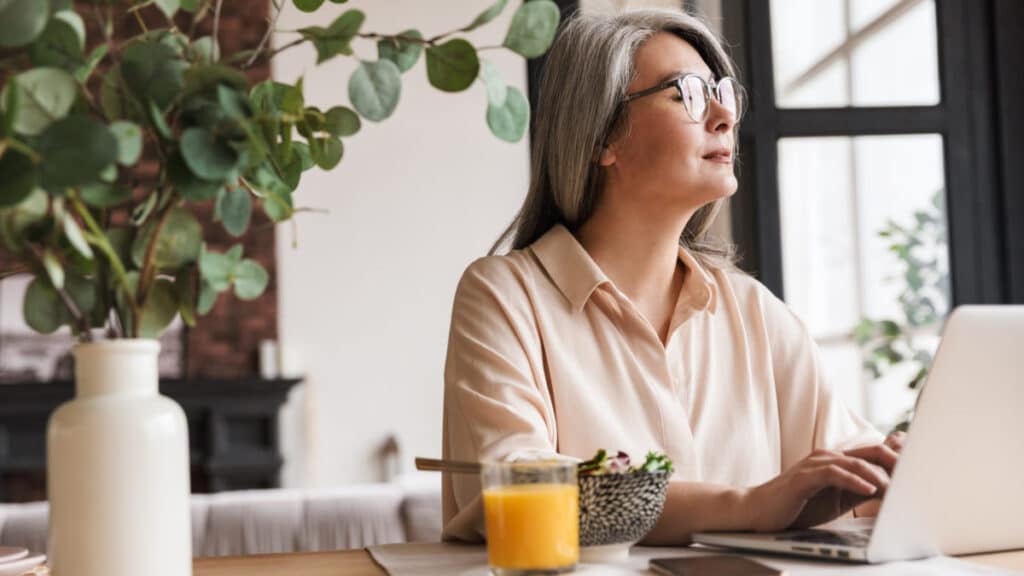 Thinking concentrated business woman Woman working on a laptop, enjoying breakfast with juice, in a bright room with plants. | Sky Rye Design Woman working on a laptop, enjoying breakfast with juice, in a bright room with plants.