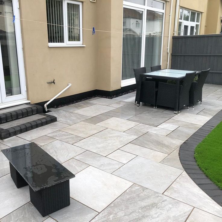 Modern patio with sleek stone tiles, outdoor dining set, and bench, creating an elegant backyard relaxation space.