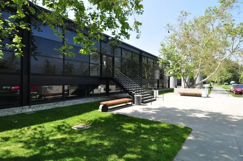 unnamed Modern glass building with a staircase, surrounded by trees and grass on a sunny day. | Sky Rye Design Modern glass building with a staircase, surrounded by trees and grass on a sunny day.