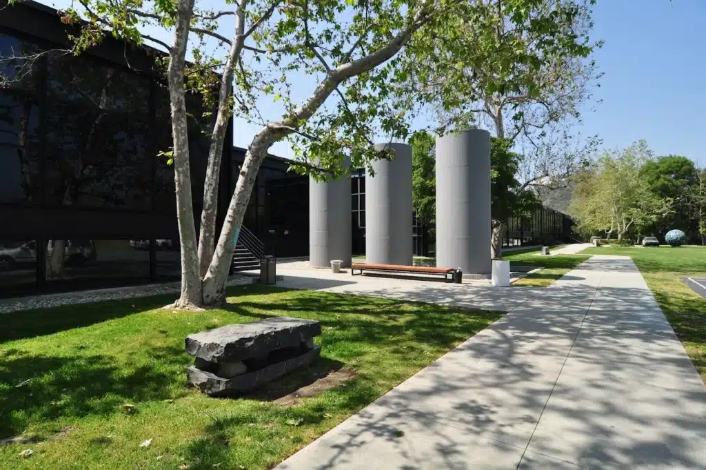 unnamed 1 Modern building exterior with large windows, trees, and a walkway on a sunny day. | Sky Rye Design Modern building exterior with large windows, trees, and a walkway on a sunny day.