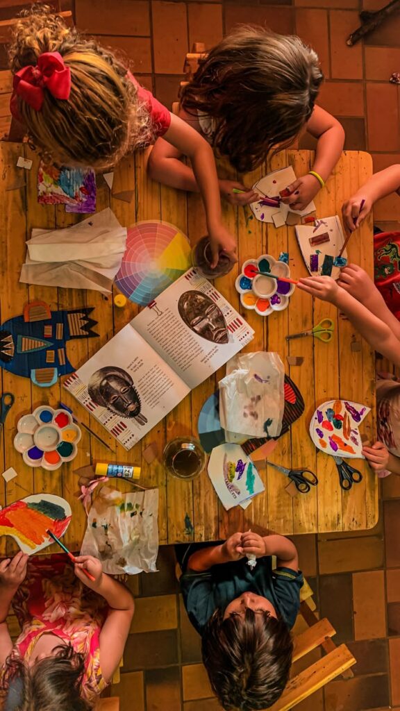 _ Children engaging in a colorful painting activity with art supplies on a wooden table. | Sky Rye Design Children engaging in a colorful painting activity with art supplies on a wooden table.