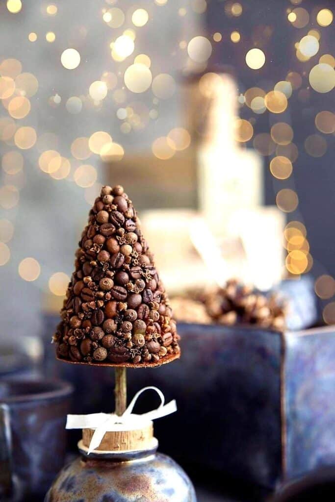 _ Christmas tree made of coffee beans with festive background bokeh lights, on a rustic stand with a ribbon. | Sky Rye Design Christmas tree made of coffee beans with festive background bokeh lights, on a rustic stand with a ribbon.