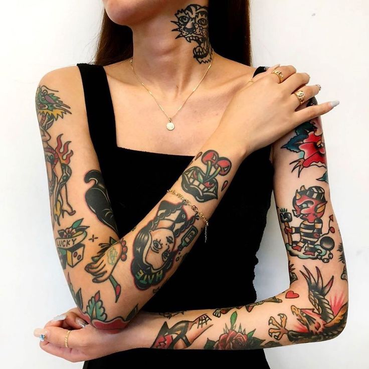 Woman in black dress with colorful sleeve tattoos featuring various designs on arms and neck.