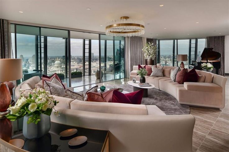 Luxurious penthouse living room with city view, featuring elegant decor, plush sofas, and a grand piano near floor-to-ceiling windows.