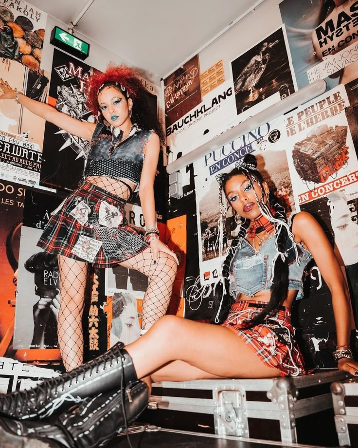 Two women in punk outfits pose in a room covered with band posters.