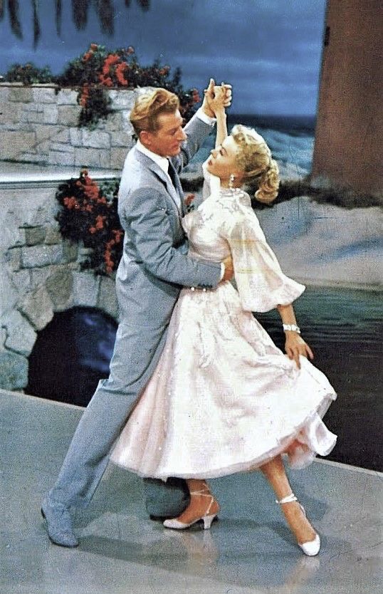 A couple elegantly dancing in formal attire, set against a scenic stone archway background.