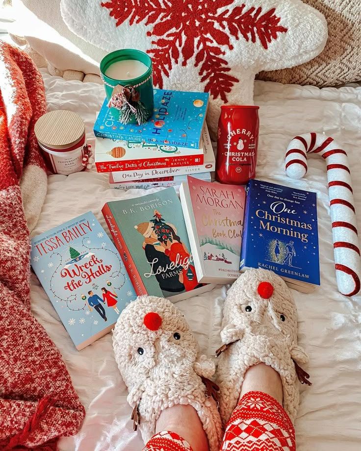 winter Cozy Christmas scene with festive books, holiday-themed slippers, a candle, and a candy cane on a bed. | Sky Rye Design Cozy Christmas scene with festive books, holiday-themed slippers, a candle, and a candy cane on a bed.