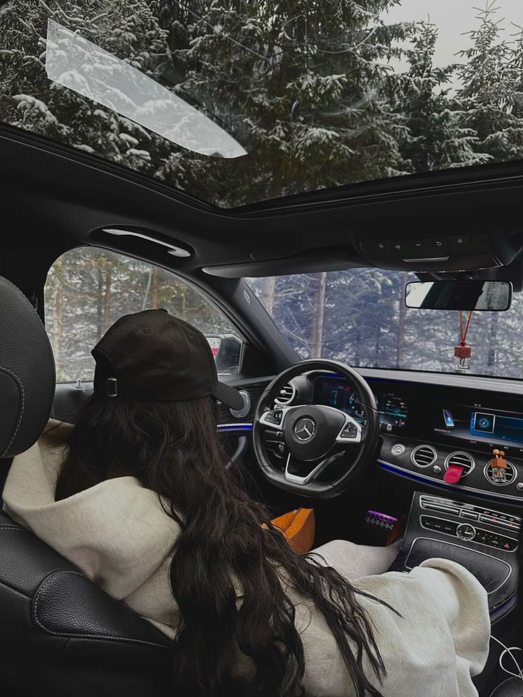 wintercarssnow Person in hoodie and cap inside a car with snowy forest view through sunroof. | Sky Rye Design Person in hoodie and cap inside a car with snowy forest view through sunroof.