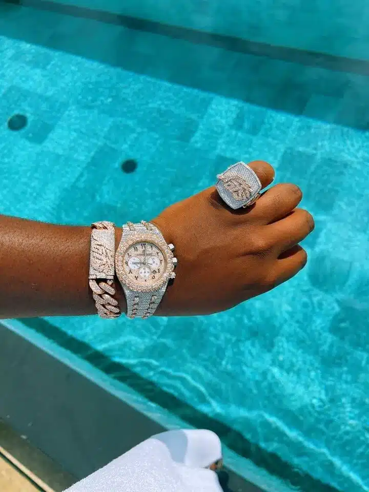 Luxurious diamond watch and jewelry on wrist near sparkling pool background.