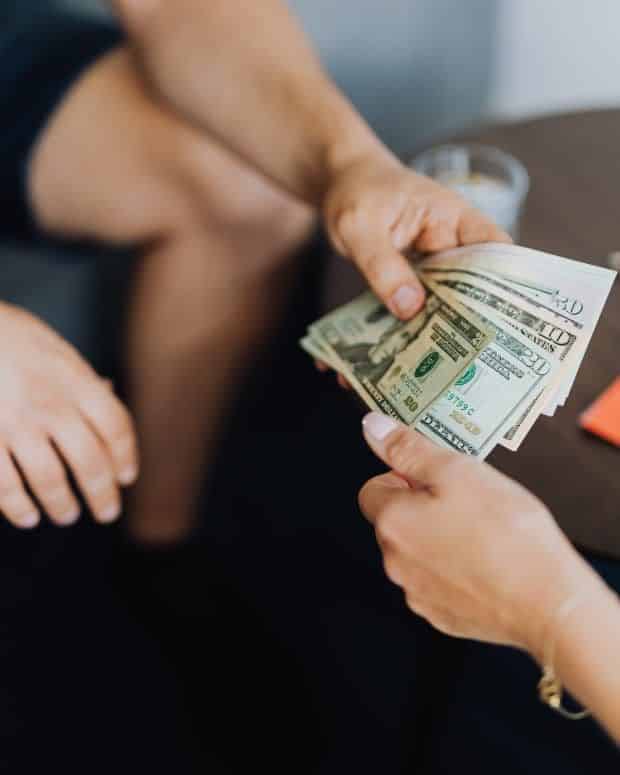 Person handing over cash, close-up on hands, financial transaction with dollar bills.