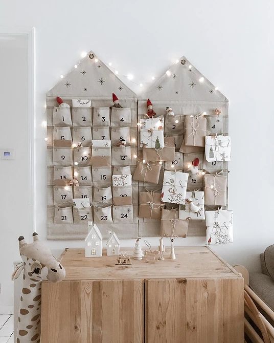 Как украсить стену на Новый год_ 7 лучших вариантов декора и идеи для разных комнат 80 фото Rustic advent calendar with wrapped gifts and twinkling lights on a wooden sideboard, featuring small decorative houses. | Sky Rye Design Rustic advent calendar with wrapped gifts and twinkling lights on a wooden sideboard, featuring small decorative houses.