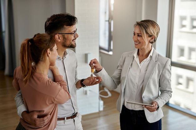 Real estate agent handing keys to happy couple in new home.