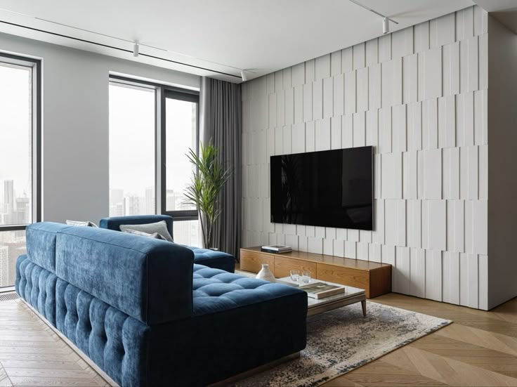 Modern living room with blue sofa, wall-mounted TV, and large windows overlooking city skyline.
