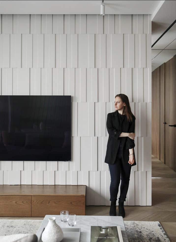 Modern living room with textured wall, TV, and a woman standing nearby, creating a stylish and cozy atmosphere.