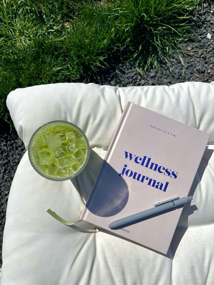 ☆ kayla Wellness journal and iced green drink on a cushion outdoors, set against green grass for a relaxing vibe. | Sky Rye Design Wellness journal and iced green drink on a cushion outdoors, set against green grass for a relaxing vibe.
