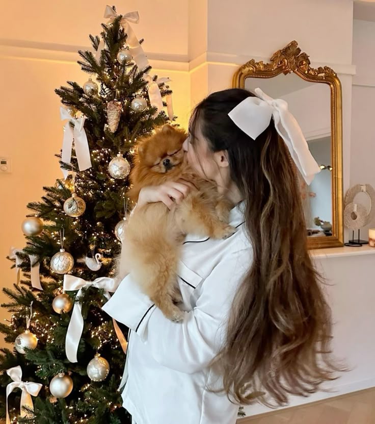 ⚡️🤍 Woman holding a Pomeranian by a decorated Christmas tree with white and gold ornaments. | Sky Rye Design Woman holding a Pomeranian by a decorated Christmas tree with white and gold ornaments.
