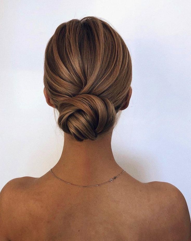 Elegant blonde updo hairstyle viewed from behind, showcasing smooth, twisted hair in a low bun against a neutral background.