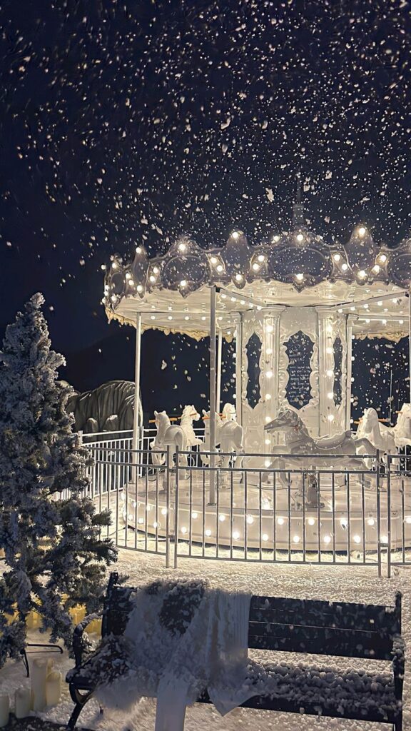 𝚙𝚊𝚎𝚌𝚓𝚢𝚢 Snowfall on illuminated carousel at night, surrounded by festive decor and a snowy bench in a winter wonderland. | Sky Rye Design Snowfall on illuminated carousel at night, surrounded by festive decor and a snowy bench in a winter wonderland.