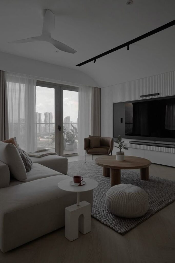 Modern living room with cozy sofa, round wooden table, and large TV, featuring neutral tones and natural light.