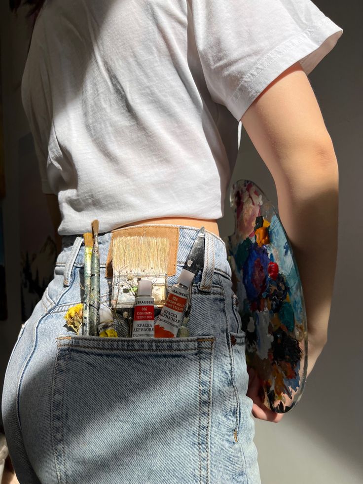 Кисти и палитра Artist with paintbrushes in jeans pocket holding a colorful palette, wearing a white t-shirt in natural light. | Sky Rye Design Artist with paintbrushes in jeans pocket holding a colorful palette, wearing a white t-shirt in natural light.