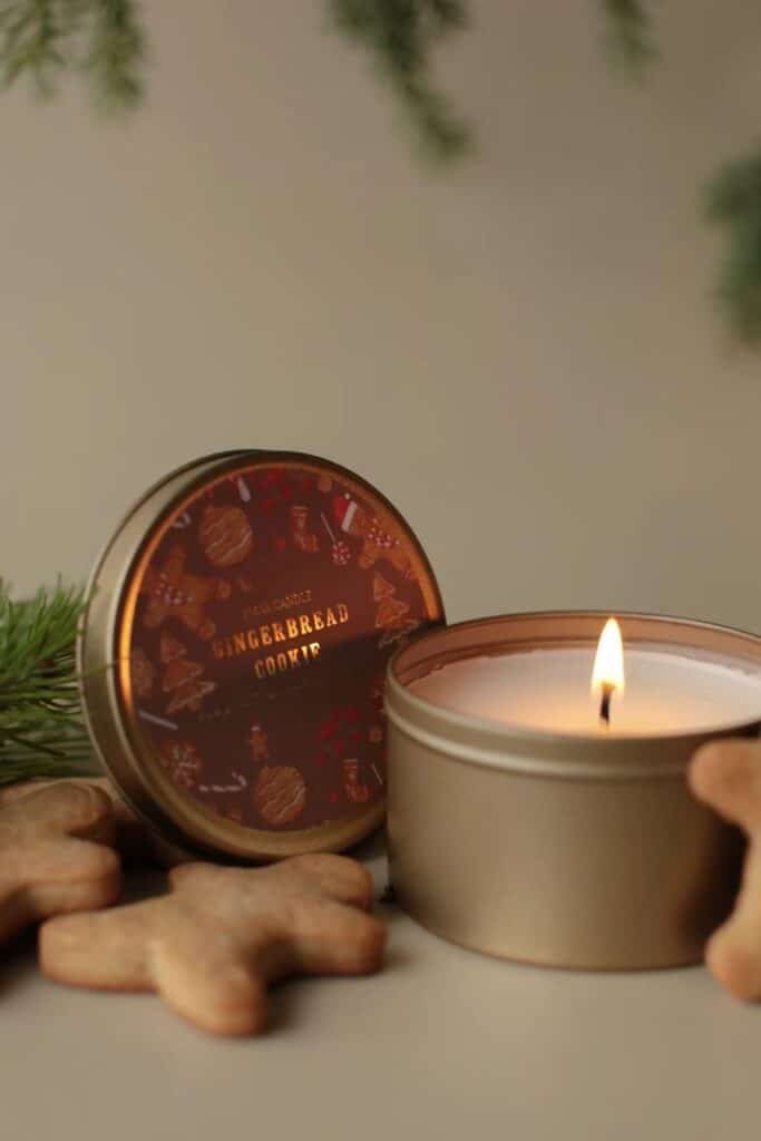 Предметная съемка свечей в новогодней тематике с еловыми ветками _ gingerbread cookie Cozy gingerbread cookie-scented candle in a tin, surrounded by festive cookies and greenery, adding warmth and charm to any space. | Sky Rye Design Cozy gingerbread cookie-scented candle in a tin, surrounded by festive cookies and greenery, adding warmth and charm to any space.