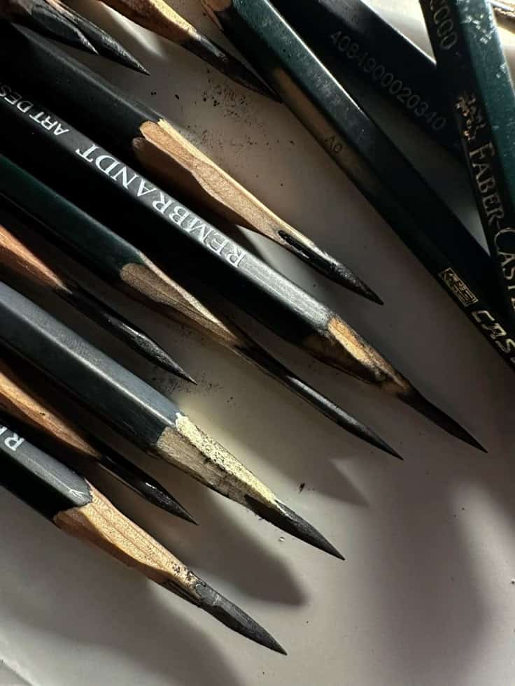 Close-up of sharpened graphite pencils on a white surface, highlighting their pointed tips and worn barrels for artistic drawing.