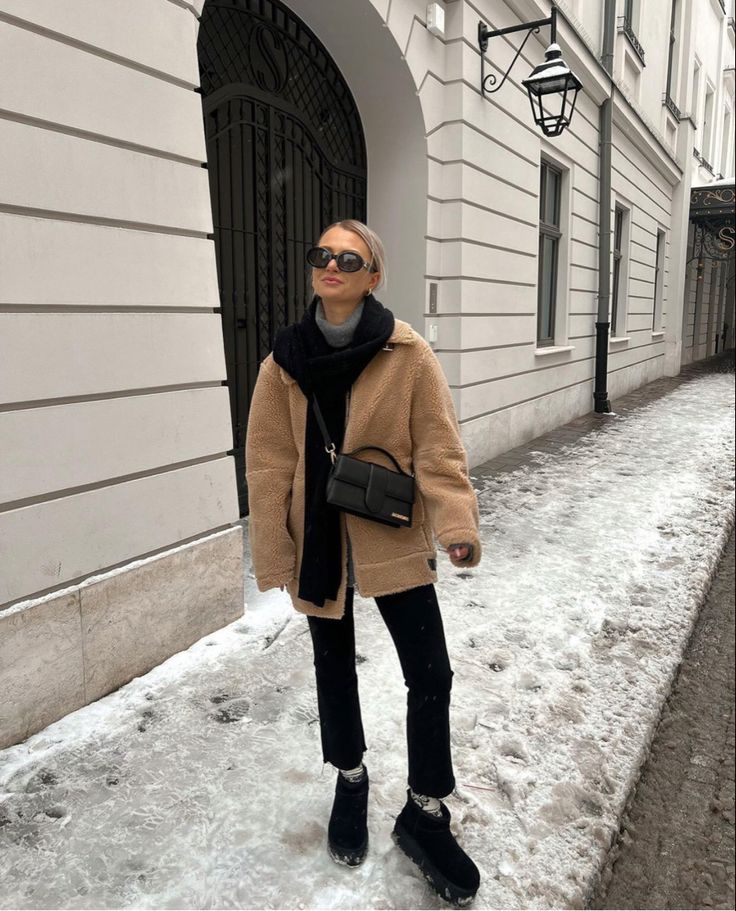 🐢 Woman in cozy winter outfit walks on snowy street, wearing a beige teddy coat, black scarf, and sunglasses, near elegant white building. | Sky Rye Design Woman in cozy winter outfit walks on snowy street, wearing a beige teddy coat, black scarf, and sunglasses, near elegant white building.