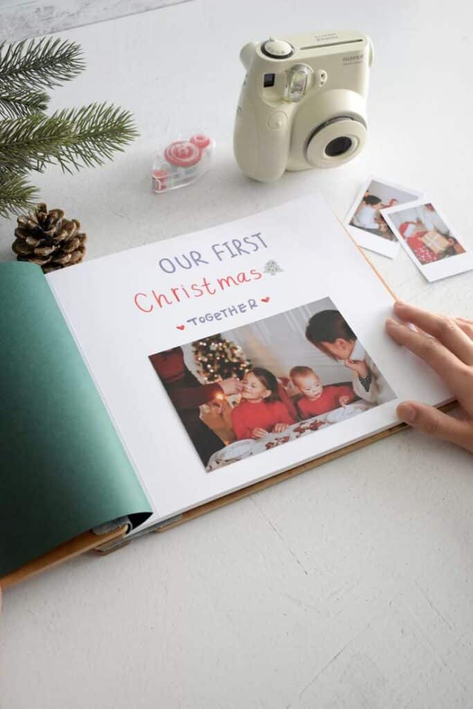Photo album page with Our First Christmas text and family photo, next to a Polaroid camera and pine decor.