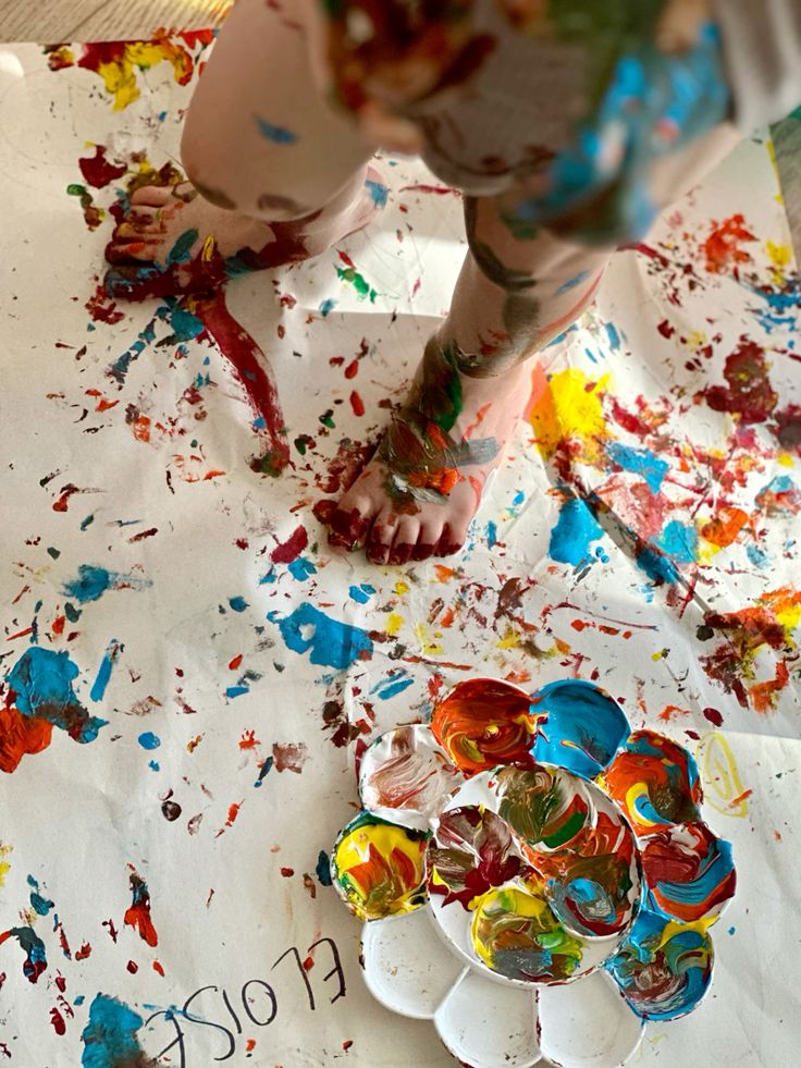 Child's feet painting on paper with colorful paint palette, vibrant creative art scene.