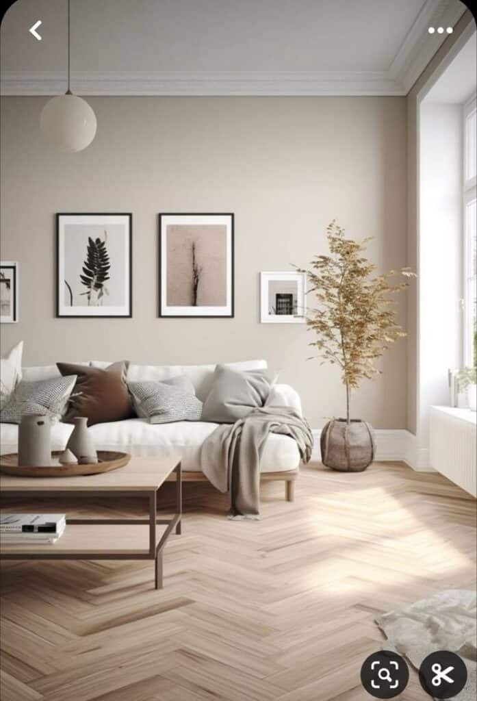 Minimalist living room with white sofa, cozy pillows, wooden coffee table, artistic wall decor, and indoor plant by large window.
