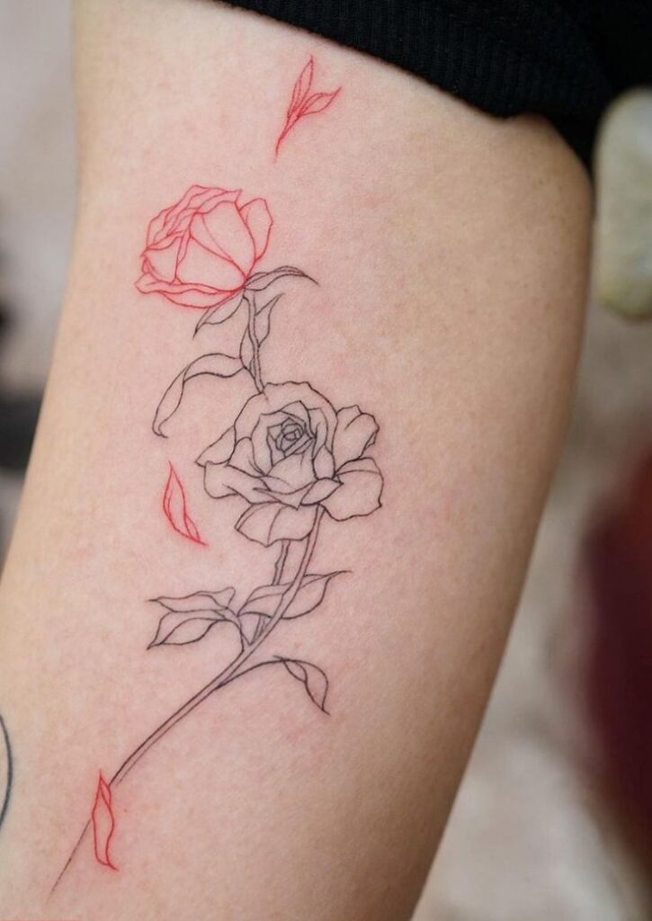Minimalist rose tattoo with red and black line art on skin, featuring delicate petals and leaves.