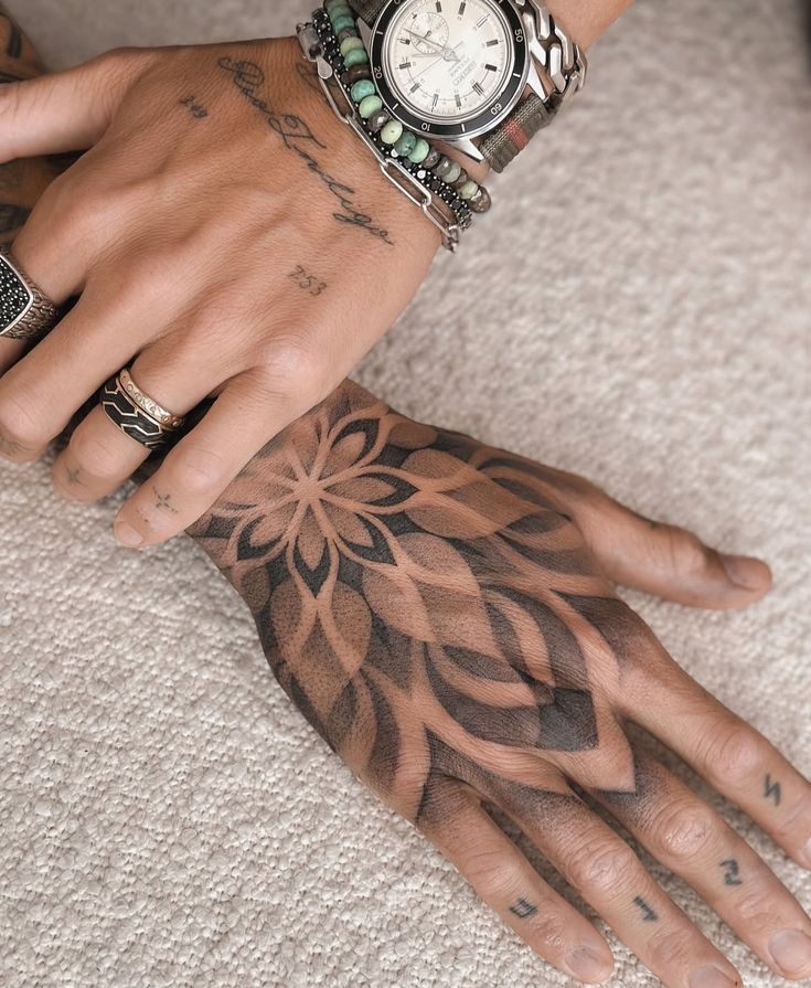 Tattooed hands with geometric design, wearing a stylish watch and bracelets on a textured surface.