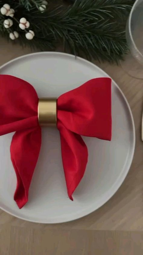 Festive table setting with a red napkin bow on a white plate, accented by evergreen branches and a gold napkin ring.