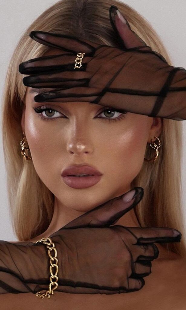 Woman with black mesh gloves and gold chain, striking pose with intense gaze and stylish earrings.