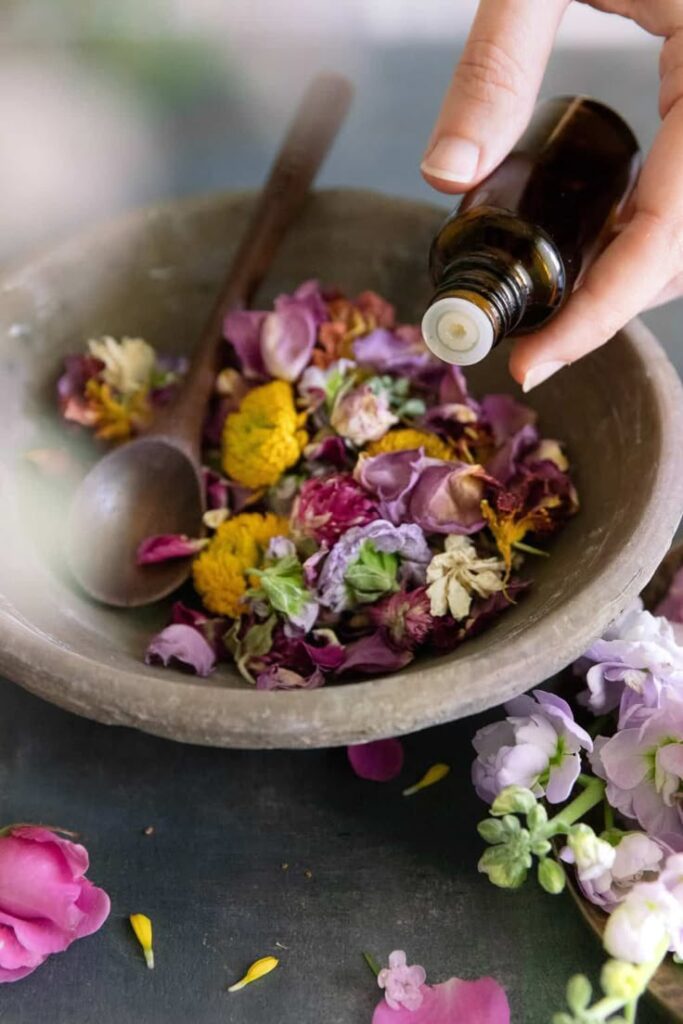 10 Natural Ways to Make Your Home Smell Like Christmas Pouring essential oil over vibrant dried flowers in a bowl, enhancing aromatherapy in a serene, natural setting. | Sky Rye Design Pouring essential oil over vibrant dried flowers in a bowl, enhancing aromatherapy in a serene, natural setting.