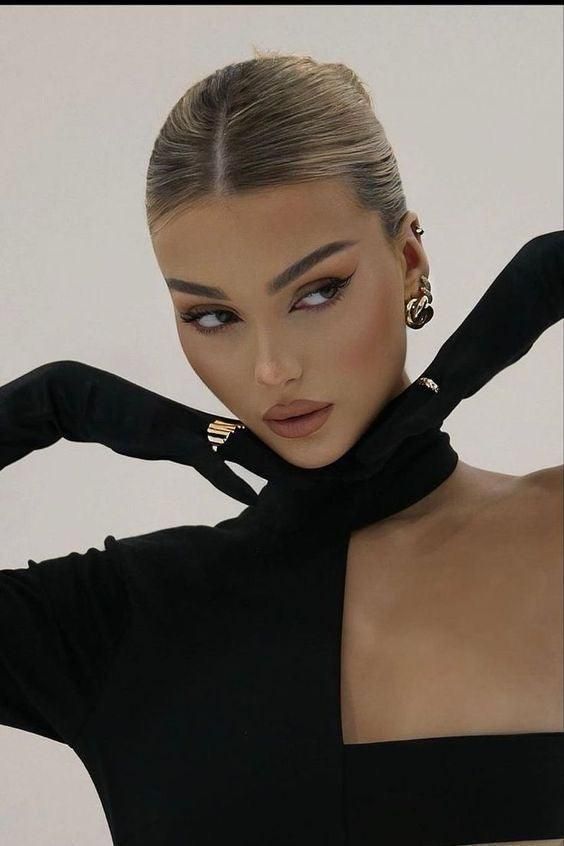 Elegant woman in black outfit with gold jewelry poses with confident gaze.