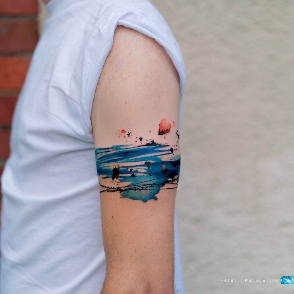 111c1b019890b9392216013ccbcd2812 Arm tattoo with abstract watercolor design in blue and red, worn by a person in a white shirt. | Sky Rye Design Arm tattoo with abstract watercolor design in blue and red, worn by a person in a white shirt.